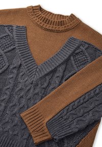 Neulottu neulepaita, jossa on v-kaula-aukko, ruskea yläosa ja tummanharmaa alaosa. Neuleessa on syvät kuvioidut palmikkokuvioinnit ja resorit hihansuissa.