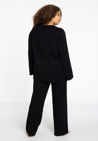 Schwarzes Langarmoberteil und weite Hose aus weichem Stoff, mit entspanntem Schnitt und minimalistischer Gestaltung ohne auffällige Muster.