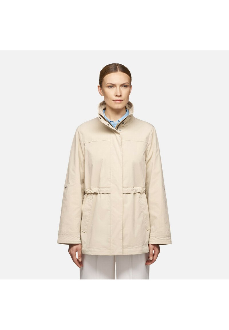 Giacca beige con colletto alto, vita elastica e maniche lunghe. Realizzata in un tessuto morbido con tasche laterali e vestibilità comoda.