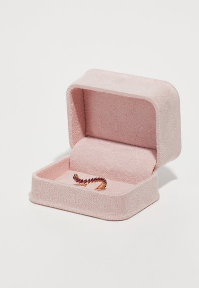 Malý zlatý prsteň s fialovými kameňmi v otvorenej mäkkej ružovej zamatovej krabici na šperky na bielom pozadí.