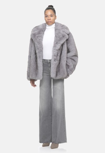 Cappotto in pelliccia sintetica grigia con ampio colletto, indossato sopra un dolcevita bianco e jeans grigi a zampa. Texture morbida e design oversize.