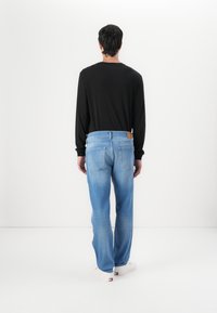 Jean bleu en denim avec une coupe droite, lavage clair et poches arrière. Associé à une chemise noire à manches longues et des chaussures blanches.