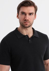 Černé polo tričko s krátkým rukávem a texturovanou tkaninou, s klasickým límcem a dvouknoflíkovou légou. Jednoduchý a dobře padnoucí design.