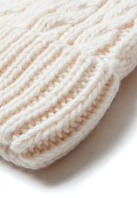 Berretto lavorato a maglia di colore crema, realizzato in filato spesso con un motivo a costine testurizzato e un dettaglio di orlo arrotolato, che offre calore e morbidezza.
