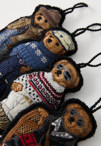 Četiri privjeska u obliku medvjeda s vezom imaju različite teksture i boje: plava, bijela, crvena i smeđa odjeća s jedinstvenim uzorcima i dodacima.
