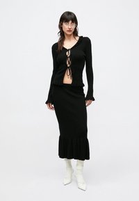 Set negru din tricot cu nervuri format din două piese, cu un top scurt cu guler cu volane și șireturi frontale, asortat cu o fustă midi cu poale cu volane.