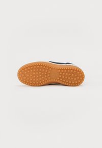 Rubberen zool met een getextureerd grippatroon, met een marineblauwe bovenkant en beige accenten aan de zijkant. Klassiek sneakerdesign.