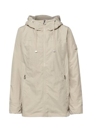 Veste à capuche beige clair avec fermeture éclair frontale, cordons de serrage réglables, poches latérales zippées et patch logo discret sur la manche gauche.