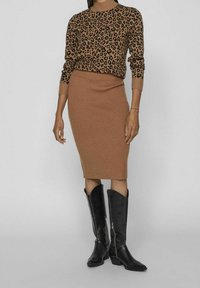 Hnědá žebrovaná pletená sukně v kombinaci s dlouhým leopardím svetrem. Modelka má na sobě černé kovbojské boty s špičatou špičkou a zipovým detailem.