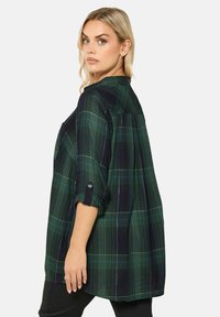 Zielona i granatowa koszula w kratę z lekkiego materiału, z guzikowym mankietem oraz luźnym krojem z plisami z tyłu dla dodatkowego detalu.