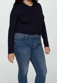 Cardigan bleu marine à manches longues avec boutons et col, porté sur un jean bleu ajusté. Tissu texturé avec une coupe classique et des détails à boutons.