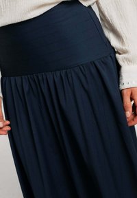 Falda azul marino con una cinturilla ancha y texturizada, y tela fruncida, que presenta un acabado suave y acentos de costura vertical.