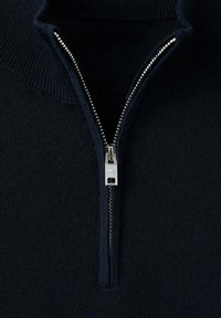 Gros plan d'un pull noir en tricot avec une fermeture éclair argentée partiellement ouverte au niveau du col.