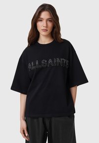 Camiseta negra de gran tamaño con mangas cortas, que presenta un logo texturizado de "ALLSAINTS" en detalle metálico en el pecho. Tela de algodón suave.