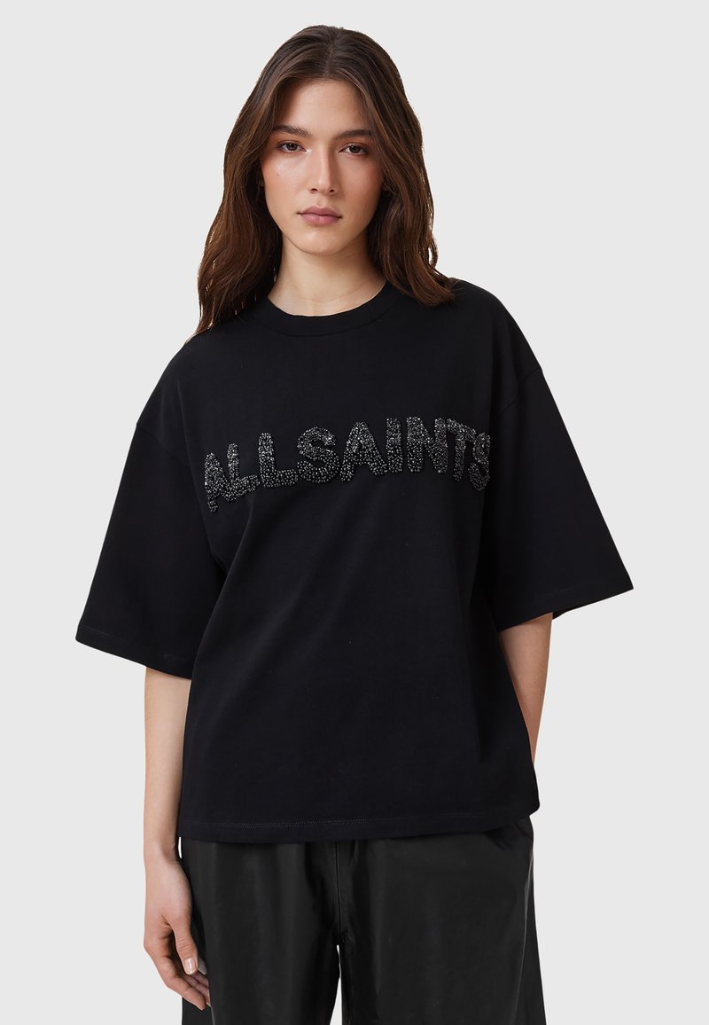 Camiseta negra de gran tamaño con mangas cortas, que presenta un logo texturizado de "ALLSAINTS" en detalle metálico en el pecho. Tela de algodón suave.