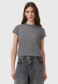 T-shirt à manches courtes rayé noir et blanc avec un col rond, associé à un jean en denim noir délavé taille haute.