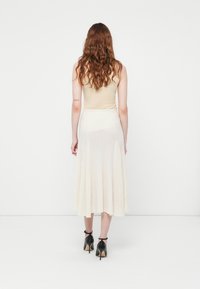 Beige tank top with a ribbed white midi skirt featuring vertical pleats, paired with black heeled shoes. No visible patterns or accents.