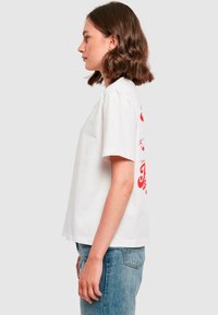 Hvid t-shirt med korte ærmer og dristig rød grafik på ryggen. Har en løs pasform og blødt bomuldsstof. Kombination med lyseblå denimjeans.
