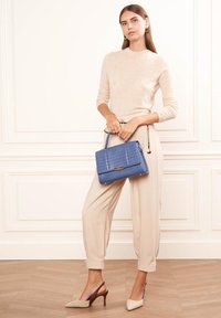 Pull en tricot beige, pantalon beige fuselé, escarpins beige clair à bouts pointus et un sac à main en faux crocodile bleu avec une bandoulière en chaîne.