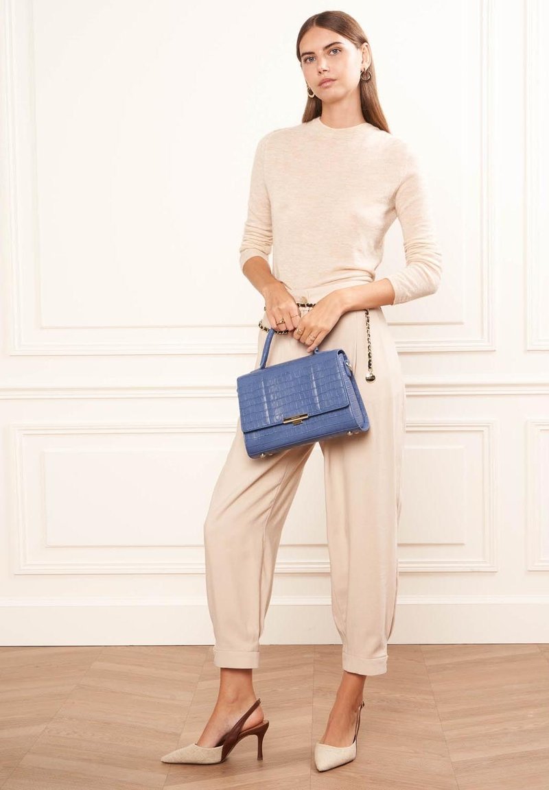 Pull en tricot beige, pantalon beige fuselé, escarpins beige clair à bouts pointus et un sac à main en faux crocodile bleu avec une bandoulière en chaîne.