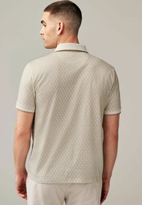 Kortærmet polo-shirt i lys beige med geometrisk mønster, kontrasterende krave og manchetter, lavet af blødt tekstilmateriale.