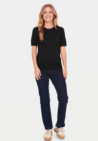Black short-sleeve knit top with a rounded neckline, paired with dark blue straight-leg jeans and beige sneakers featuring green accents.