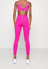 Leggings de entrenamiento de un brillante color rosa y sujetador deportivo a juego con un diseño de espalda baja, que presentan detalles azules en la pierna y un ajuste ceñido.