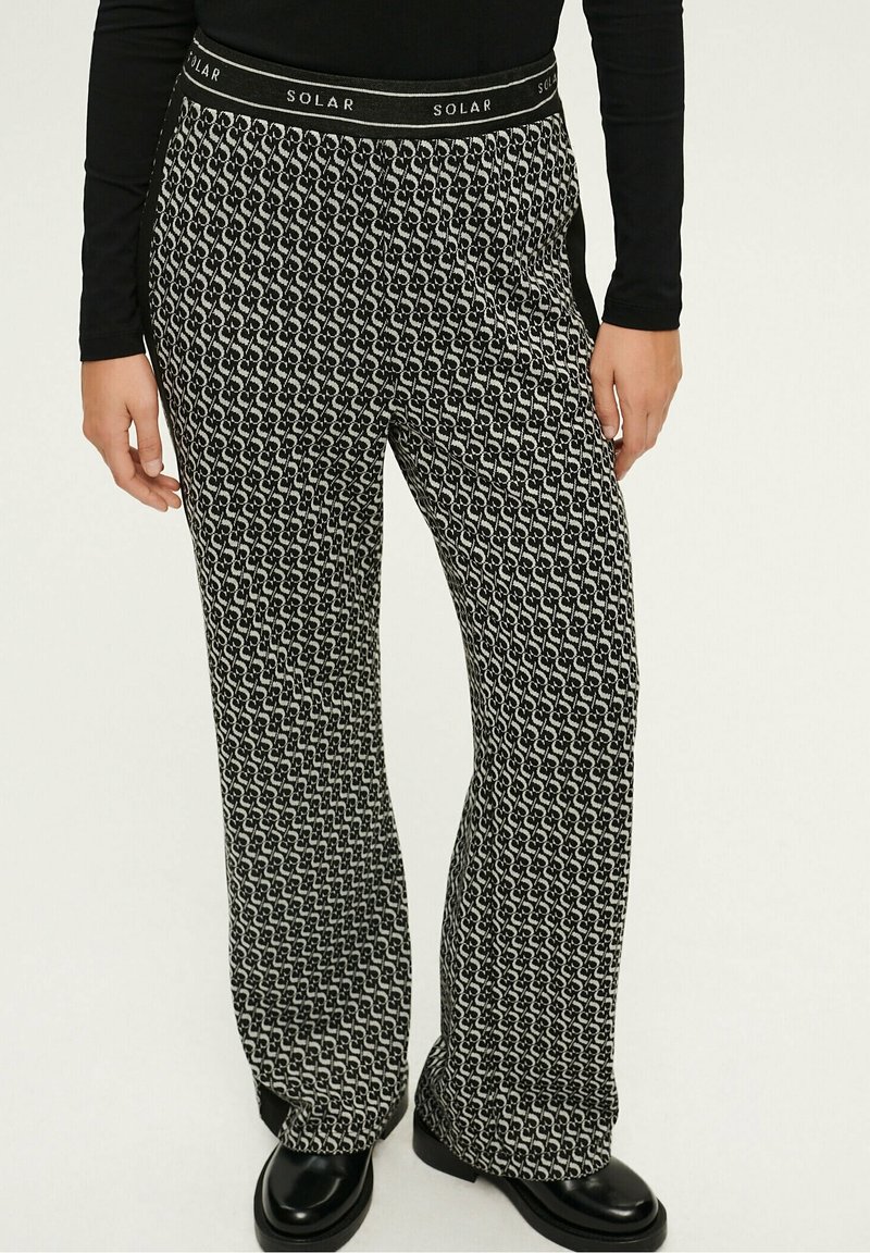 Pantalon large à motif noir et blanc avec taille élastique portant l'étiquette "SOLAR", porté avec un haut noir et des chaussures noires.