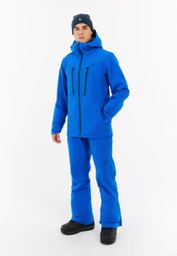 Modrá vonkajšia bunda a nohavice vyrobené z nepremokavého materiálu, s vreckami na zips, kapucňou a pevným čiernym obuvím. Čistý dizajn, funkčné.