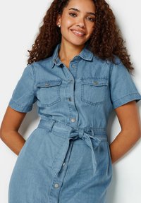 Denim-paitapaita mekko vaaleansinisena, lyhyet hihat, napit edessä, kaksi rintataskua, kapea vyötärö sitomisvyöllä, sileä pinta.