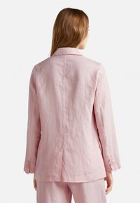 Blazer de lino rosa claro con solapa, mangas largas y puños abotonados. Tejido texturizado con un corte relajado y detalle de abertura en la parte trasera.