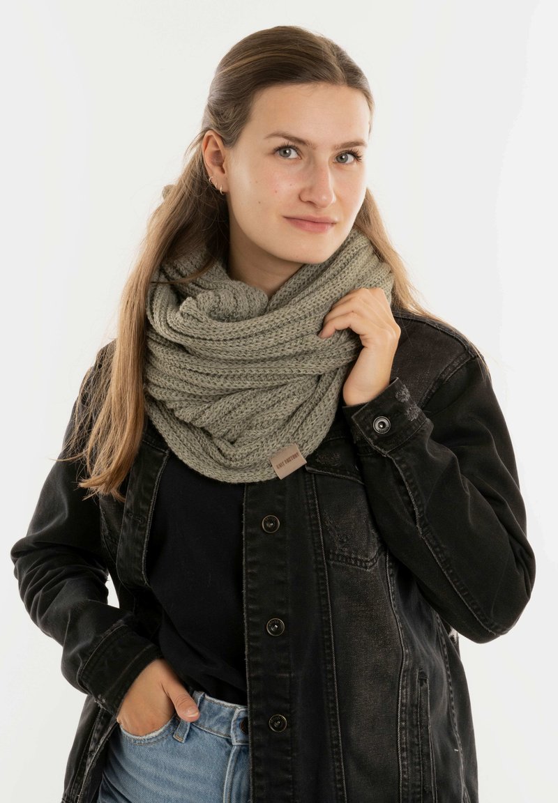 Lichtgroene gebreide infinity sjaal met een textuurpatroon. Gecombineerd met een zwarte denimjack en een zwart topje. Casual gedragen.