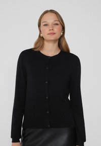 Schwarzer Cardigan mit Rundhalsausschnitt, langen Ärmeln und durchgehender Knopfleiste. Weiche Textur und dezentes Strickmuster. Angenehmer Sitz an der Taille.