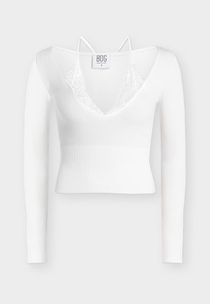 Witte geribde cropped top met lange mouwen, diepe V-hals, kanten afwerking en dunne schouderbandjes op een effen achtergrond.