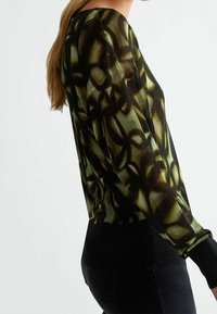 Pitkähihainen neule, jossa on musta- ja vihreä abstrakti kuvio, teksturoidusta kankaasta ja musta ribbineuloshelma.