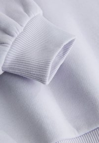 Svetlofialová mikinová látka s rebrovanými manžetami a hladkým povrchom, zdôrazňujúca textúru a jemné farebné variácie.