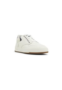 White sneakers with textured upper, round toe, navy accents, and padded tongue. Features white laces and a light brown rubber sole.