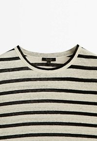 Randig t-shirt med rund halsringning, tillverkad av lätt tyg. Har växelvis svarta och krämfärgade horisontella ränder. Etikett synlig inuti.