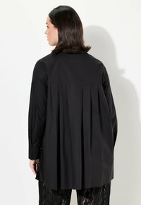 Camicia nera con maniche lunghe, dettaglio plissè sulla schiena e polsini con bottoni. Tessuto liscio con colletto classico e design a taglio dritto.