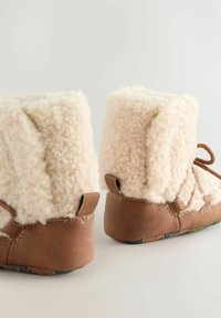 Braune Wildleder-Booties mit einem weichen cremefarbenen Schaffell-Obermaterial, das einen gefalteten Bund und ein einfaches Bindeband aufweist. Flache Sohle und lässiges Design.