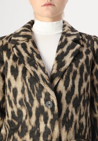 Abrigo de lana con estampado de leopardo en negro y beige, que presenta un cuello con muesca y un cierre de un solo botón negro.