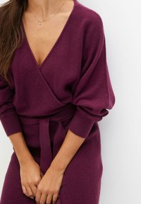 Maglione avvolgente viola con maniche lunghe e voluminose, texture a coste e una cintura abbinata. Il design a V mette in risalto il collo.