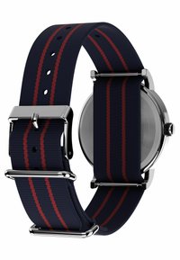 Marineblå nylon urrem med røde striber, sølvhardware og rektangulært spænde. Tekstureret overflade og flere justeringshuller for pasform.