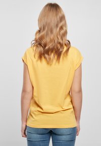 Žluté tričko s krátkým rukávem a volným střihem, vyrobené z měkké látky. Design má kulatý výstřih a rovný lem.