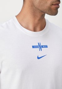 Weißes T-Shirt aus Baumwolle mit rundem Ausschnitt, versehen mit einem blauen Grafikdesign mit "ENG" und dem Nike-Logo auf der Brust.