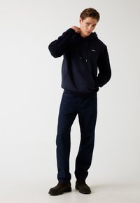 Felpa con cappuccio navy con maniche a treccia e tasca anteriore a marsupio, abbinata a jeans blu scuro e stivali neri con lacci.