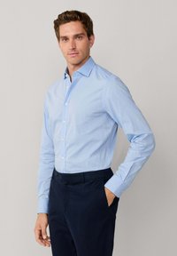 Lichtblauw overhemd met knopen en een subtiel stippenpatroon, klassieke kraag, lange mouwen en een getailleerde pasvorm, gecombineerd met donkere broek.