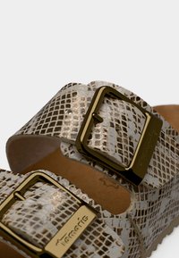 Gros plan sur des brides de sandales à motif peau de serpent beige et marron avec des boucles dorées et le logo Tamaris embossé.