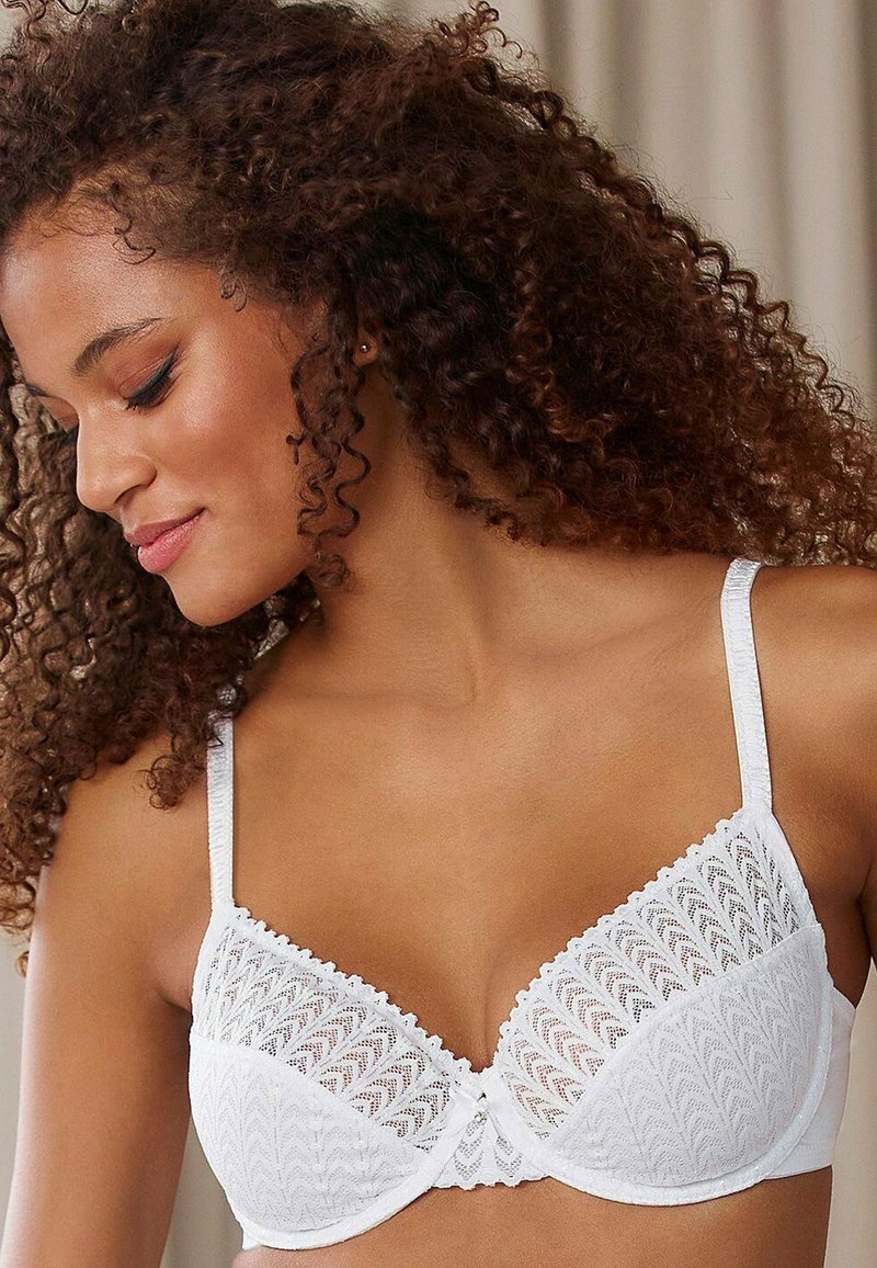Witte kanten bralette met geschulpte randen, een gestructureerd patroon op de cups, verstelbare bandjes en een klein centraal versieringsdetail.