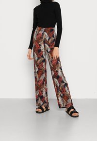Pantalon fluide à jambes larges avec un fond sombre et un motif de feuilles multicolores, associé à un col roulé noir cintré et des sandales épaisses.